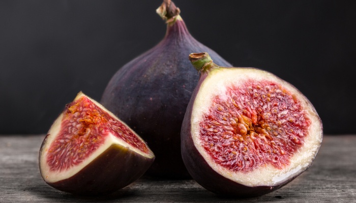 A sliced ripe fig and a whole fig on a wood table.