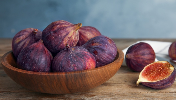 A wooden bowl of figs on a table beside a fig that has been sliced open.